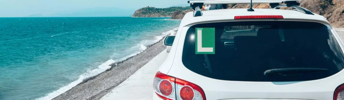 Coche blanco con la L de conductor novel en la playa